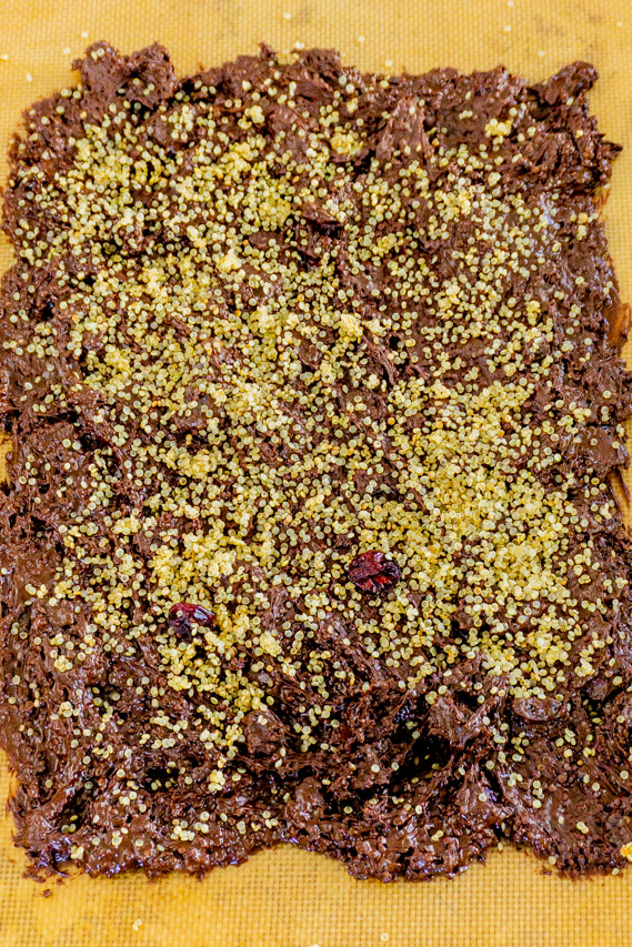 Mix most of the quinoa cranberry mixture into the chocolate. Add this chocolate quinoa mixture to the parchment-lined baking sheet and spread it evenly until desired thickness. Sprinkle the rest of the quinoa cranberry mixture on top.